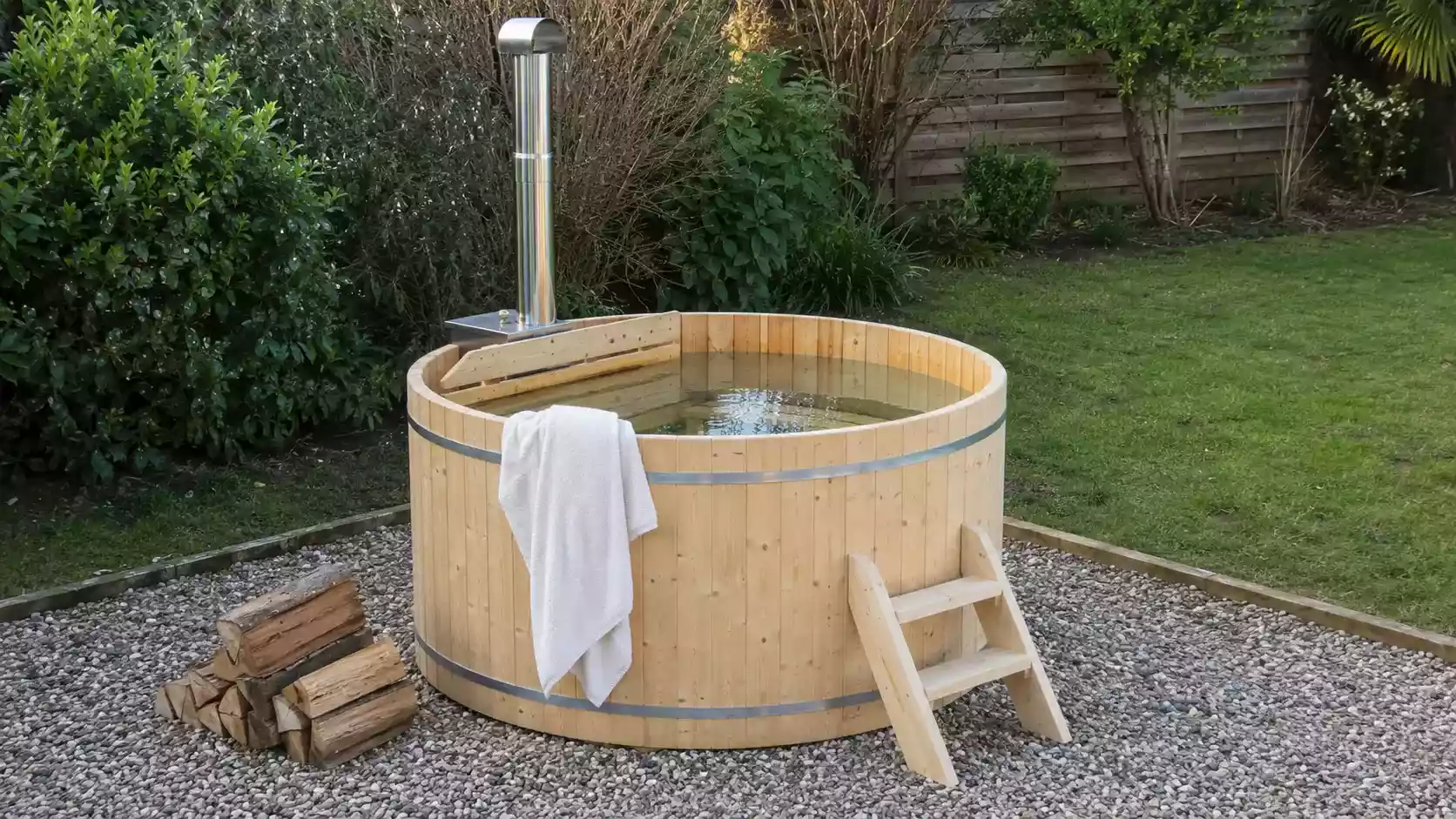 Spa nordique Finntherm Bergen en épicéa dans un jardin, avec poêle à bois et bûches
