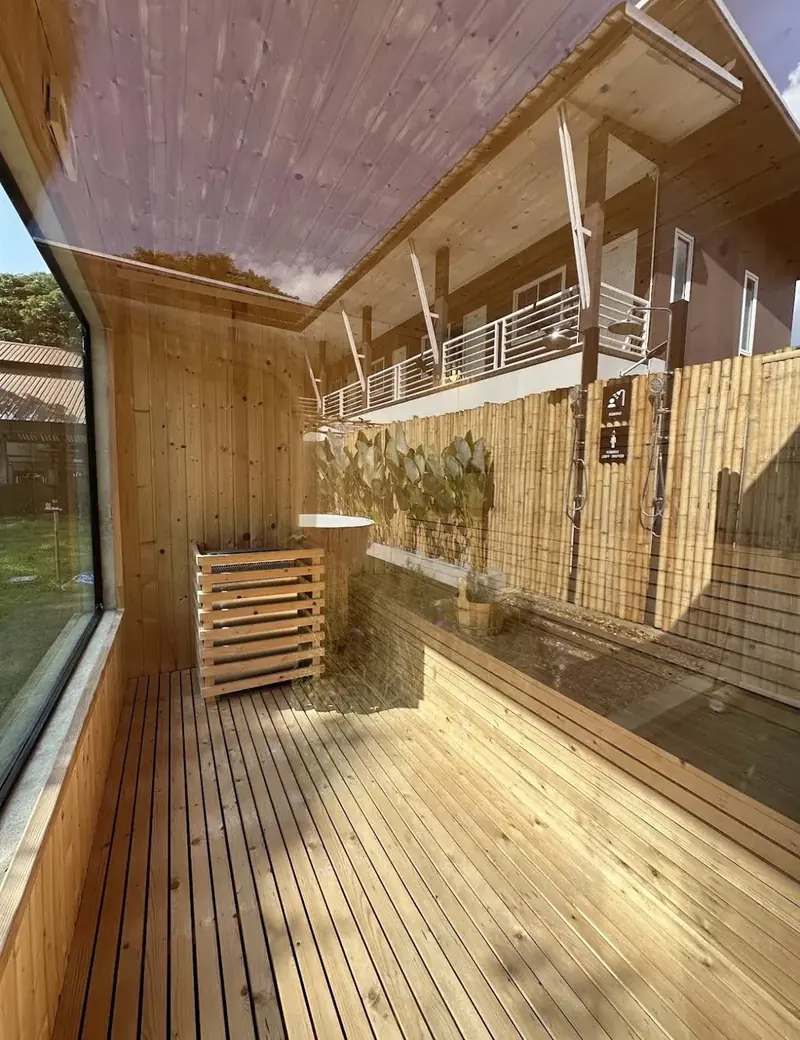 Terrasse en bois vue depuis un sauna, avec bassin d'eau froide et douches extérieures