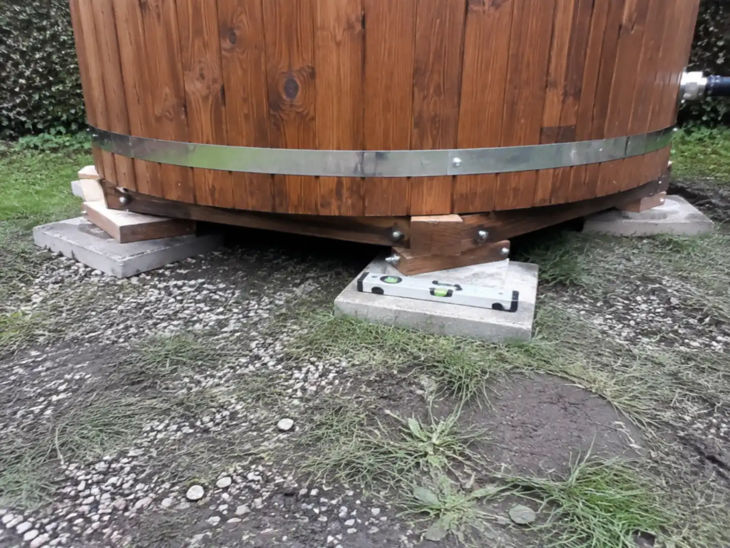Base d’un bain nordique en bois reposant sur des plots béton, avec un niveau à bulle posé sur l’un des plots