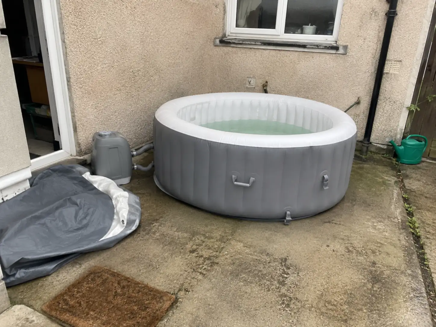 Spa gonflable gris et blanc posé sur une terrasse béton avec son bloc de filtration et sa housse repliée au sol