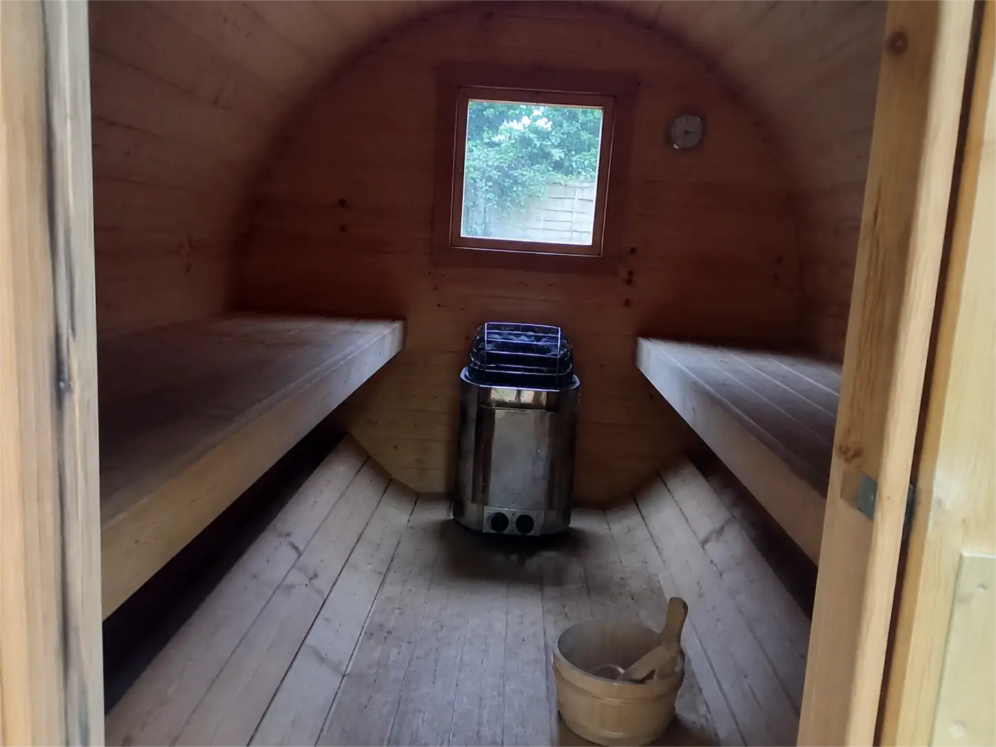 Intérieur d'un sauna tonneau avec ses deux niveaux de banquettes, son poêle et son bac de pierres