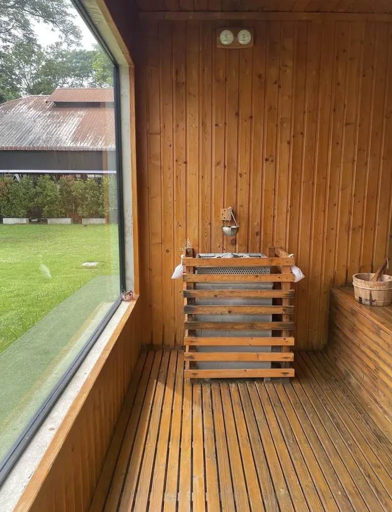 Intérieur d'un sauna en bois avec poêle électrique protégé par des lattes, seau et louche