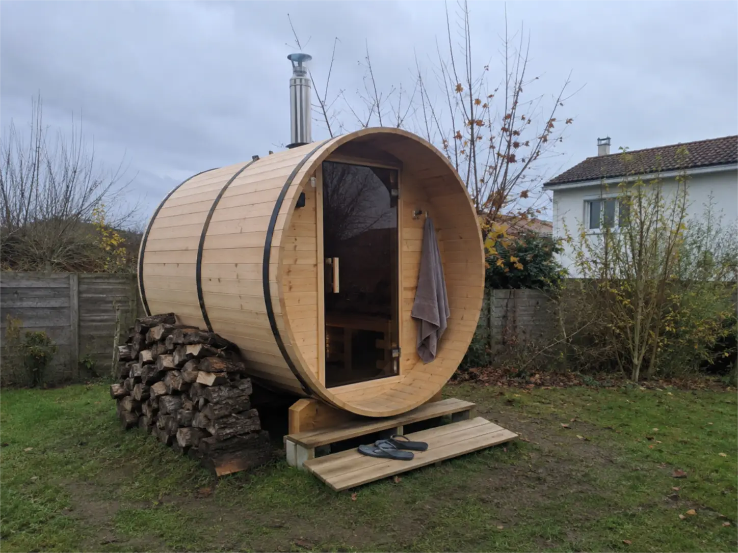 Sauna tonneau extérieur en bois avec poêle à bois et réserve de bûches dans un jardin