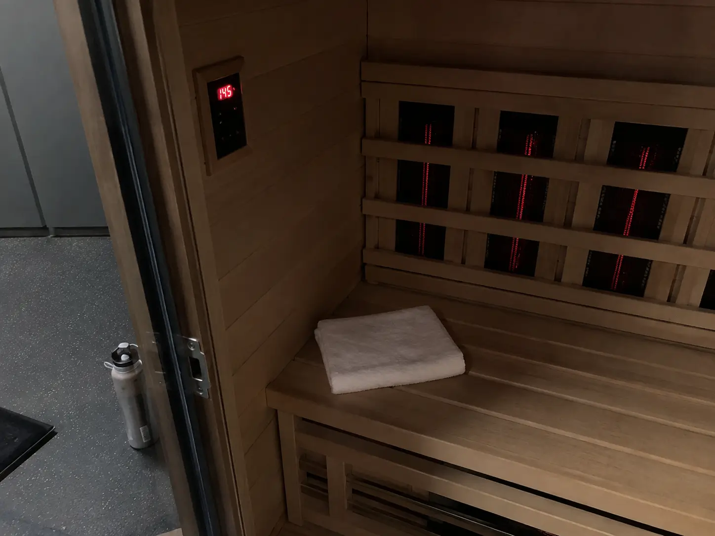 Intérieur d’une cabine de sauna infrarouge en bois de hemlock, banc avec serviette et écran de température réglé à 55 degrés