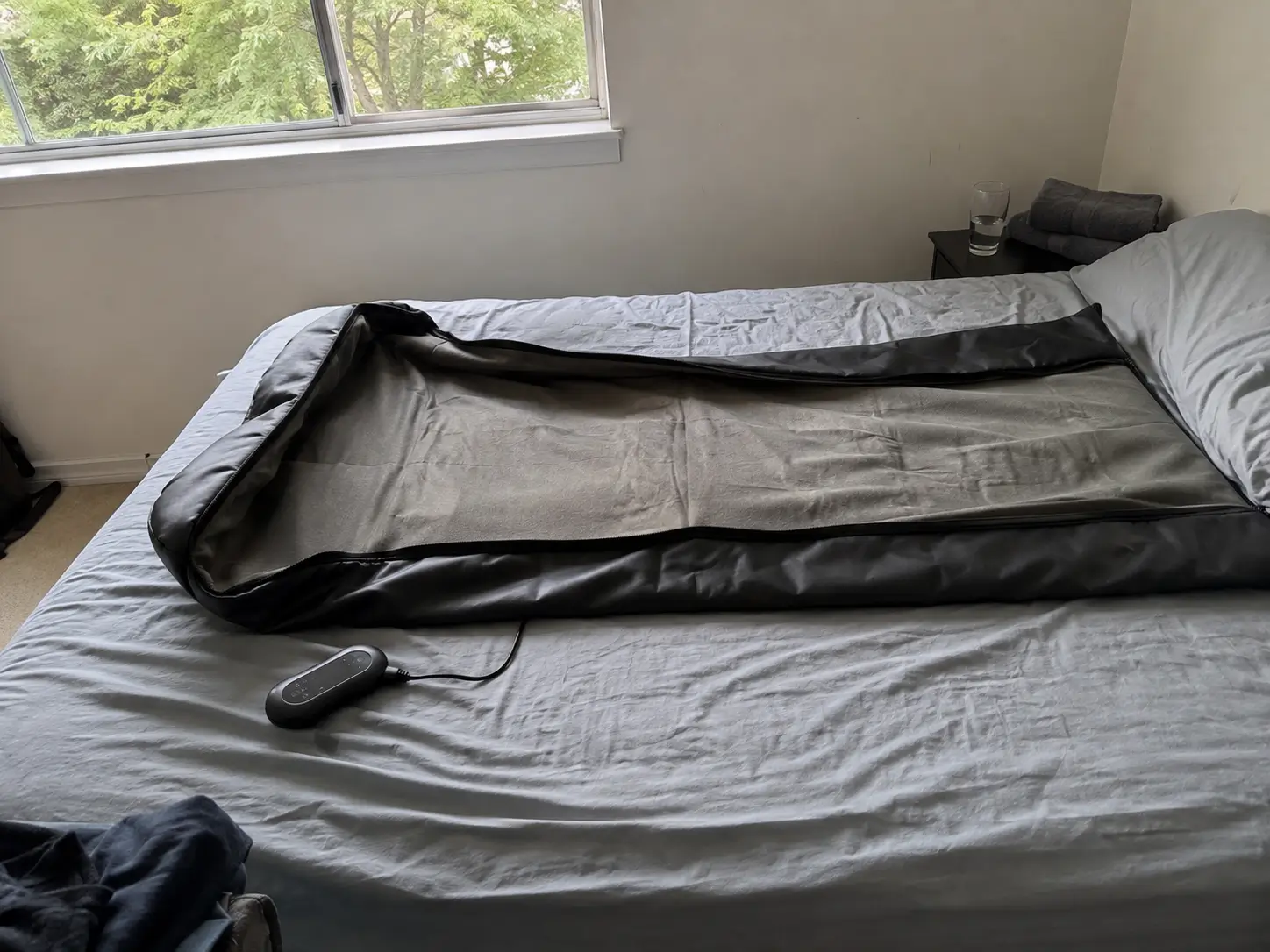 Couverture de sauna infrarouge dépliée sur un lit, boîtier de commande et verre d’eau posés à côté