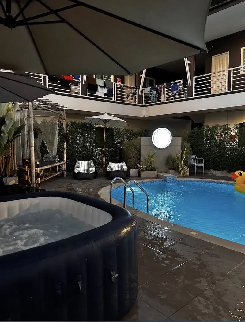 Spa gonflable noir en eau chaude à côté d'une piscine éclairée, de nuit